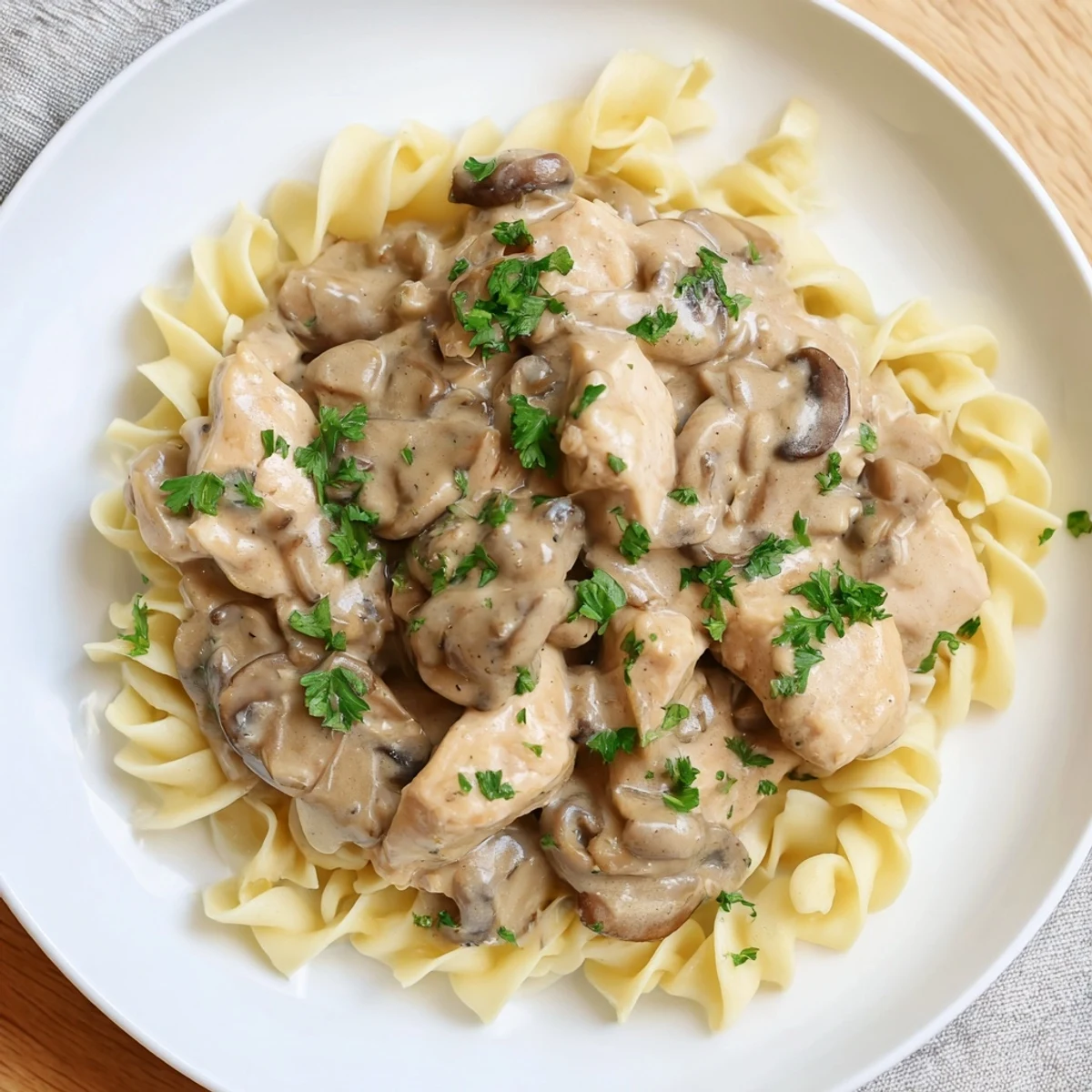 A bowl of creamy chicken stroganoff, garnished with parsley and served over fluffy egg noodles.