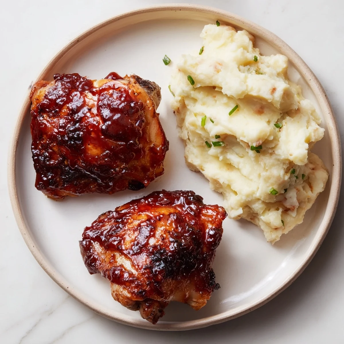 Golden-brown honey BBQ chicken thighs glistening, served with fluffy garlic mashed potatoes for dinner.