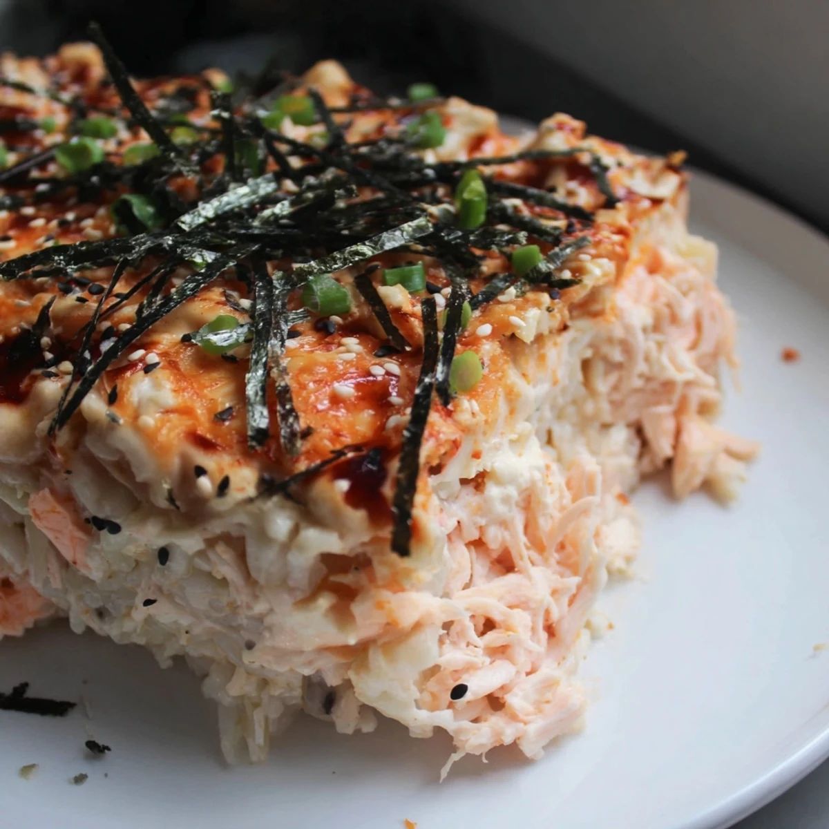 Creamy Salmon Sushi Bake topped with melted cheese, sesame seeds, and green onions, ready to scoop.