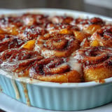 Warm Peach Cobbler Cinnamon Roll Casserole with melted icing and pecans.