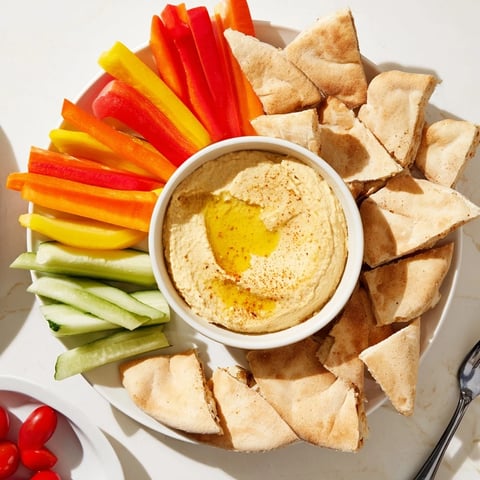 Creamy DIY hummus surrounded by warm pita bread and vibrant veggie sticks, ready to dip.