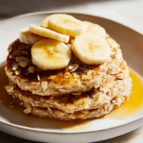 Golden-brown banana oat pancakes stacked high, drizzled with maple syrup; a delicious breakfast.