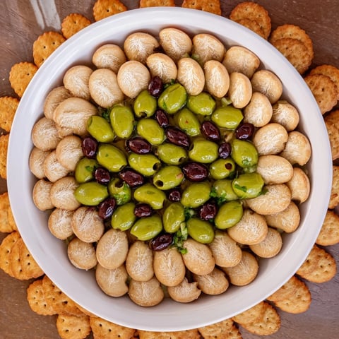 Close-up view of The Roman Colosseum Snack Platter displaying olives as gladiators in a cracker arena.