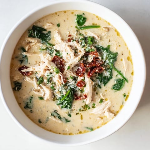 Creamy Tuscan Chicken Soup in a rustic bowl, garnished with fresh spinach and sun-dried tomatoes beside crusty bread.  