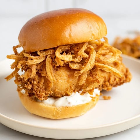Golden crispy chicken thigh on a toasted brioche bun, topped with crunchy fried onions and creamy aioli.