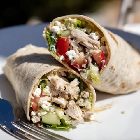 Freshly rolled Greek Lemon Chicken Salad Wrap with juicy chicken, crisp vegetables, and feta cheese on a plate.