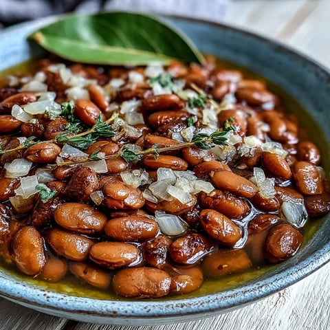 Creamy, tender pinto beans simmered with onions and garlic in a rustic pot, ready to serve as a hearty side dish.