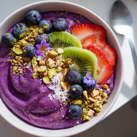 Colorful smoothie bowl showcasing purple yam, pistachios, and crunchy granola toppings.  