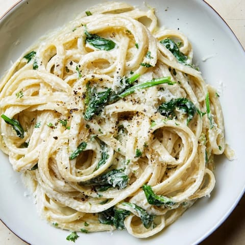 A steaming bowl of Creamy Greek Yogurt Spinach Alfredo Pasta, topped with fresh Parmesan and pepper.