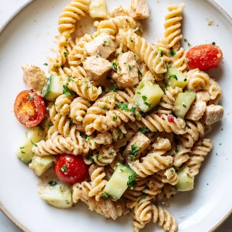 A close-up of Honey Mustard Chicken Pasta Salad, fresh greens and tomatoes peek from under tender chicken and pasta.