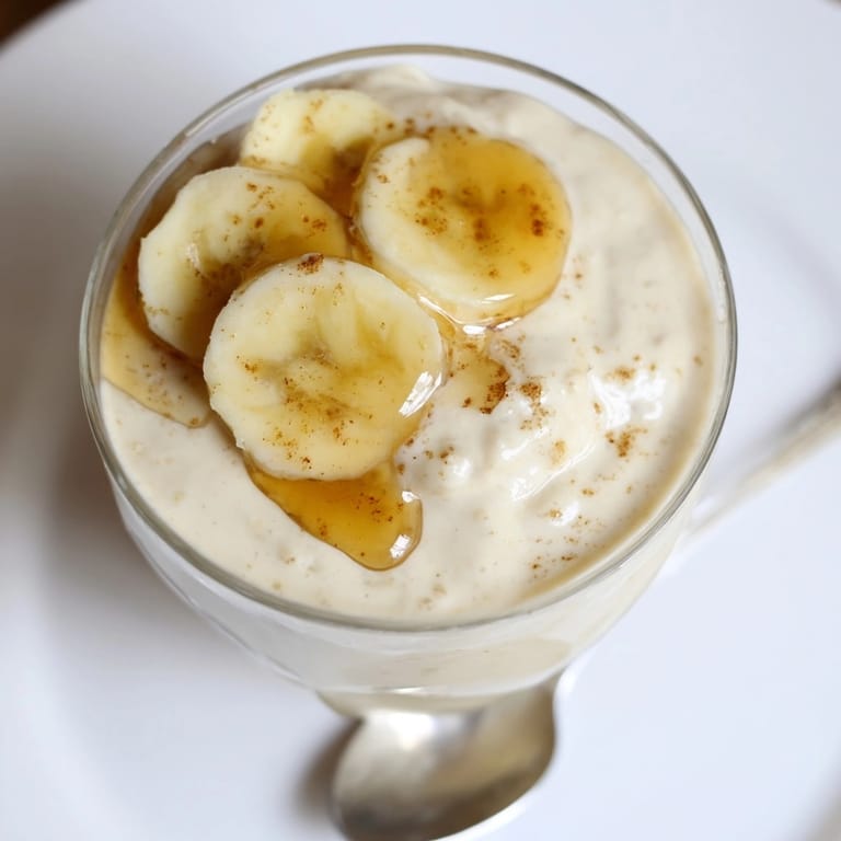 Close-up of a Honey Banana Smoothie in a glass, topped with sliced bananas.